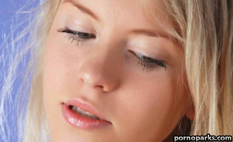 Close-up of a blonde woman with eyes closed and lips slightly parted against a blue background.